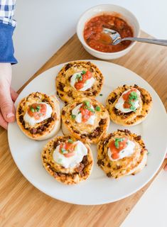 a person holding a plate with mini pizzas on it next to a bowl of chili