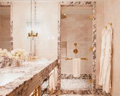 a bathroom with marble walls and flooring, gold fixtures and white towels hanging on the wall