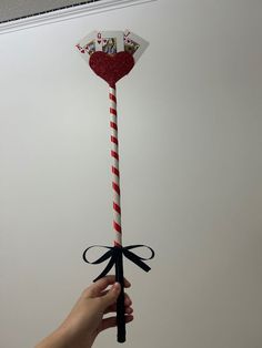 a hand holding up a candy cane with a heart on it's top and ribbon