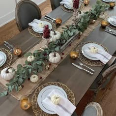 the table is set with white pumpkins, greenery and silverware on it