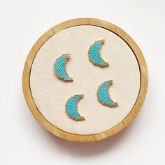 three small blue and white earrings in a wooden frame on a table top with beading