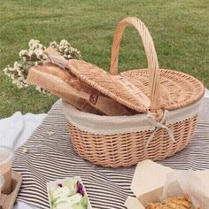 a picnic basket with bread and other food on a blanket in front of some grass