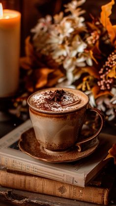 a cup of hot chocolate sitting on top of a book next to a candle