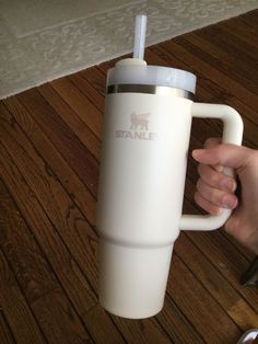 a person holding a white coffee cup on top of a wooden floor