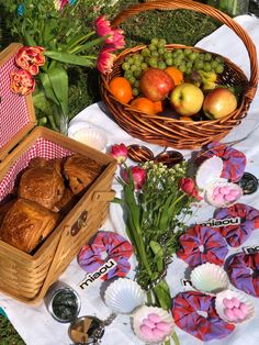 an assortment of fruit and pastries on a picnic blanket next to baskets of flowers