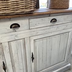 an old white cabinet with two baskets on top