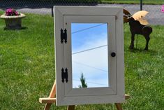 a small white wooden cabinet with a mirror on it's side in the grass