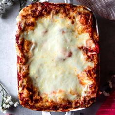 a square pizza with cheese and sauce on it sitting on a plate next to flowers