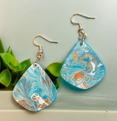 a pair of earrings with blue and orange designs on them sitting next to a potted plant