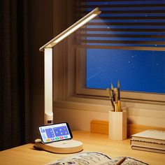 an electronic device is sitting on a desk next to a book, pencils and pen