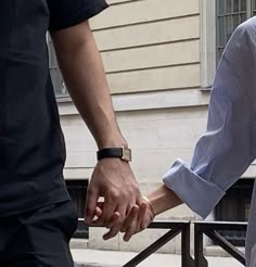 two people holding hands while standing next to each other in front of a white building