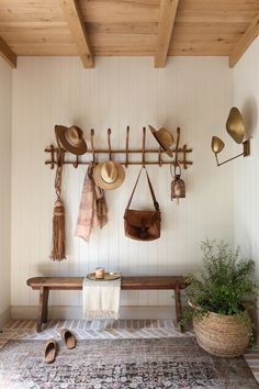 a wooden bench with hats hanging from it's hooks on the wall next to a rug and potted plant