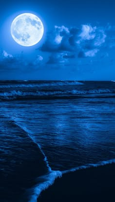 a full moon is seen over the ocean on a cloudy night with waves lapping in front of it