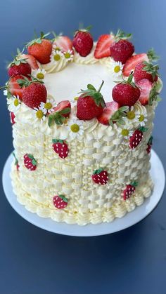 a white cake with strawberries on it sitting on a blue tablecloth covered plate