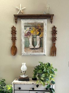 an old dresser with flowers and utensils on it in front of a painting