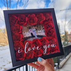 a person holding up a frame with roses in the shape of a heart and i love you written on it