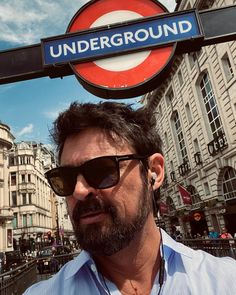 a man wearing sunglasses standing under an underground sign