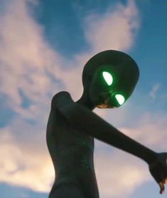 an alien statue with glowing green eyes and hands in front of a cloudy blue sky