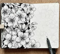 a black and white drawing of flowers on a notebook with a pen next to it