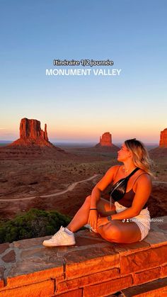 a woman sitting on top of a brick wall in front of the desert and mountains