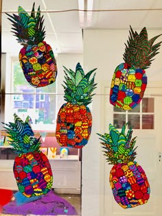 three pineapples are hanging from the ceiling in front of a window with colorful decorations