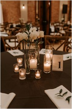 a table with candles and flowers in vases next to napkins on the table