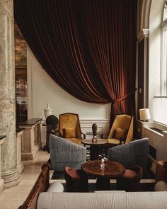 a living room filled with furniture next to a window covered in red curtained drapes