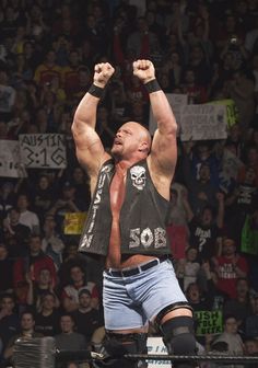 a man standing on top of a wrestling ring holding his hands up in the air