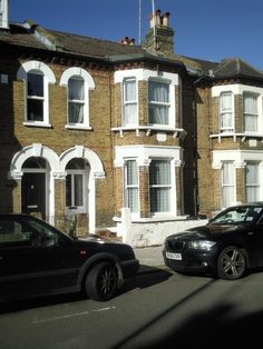 two cars parked in front of a row of brick houses with white windows and shutters