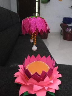 a pink paper flower sitting on top of a black couch next to a lamp shade