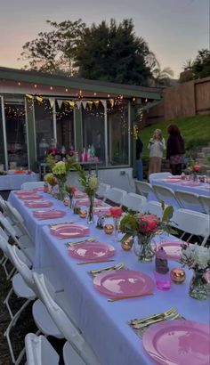 a table set up with pink plates and place settings for an outdoor dinner party at dusk