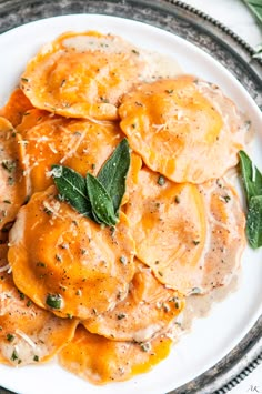 a white plate topped with ravioli covered in sauce and cheese, garnished with green leaves