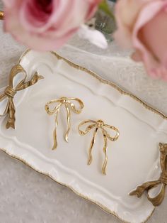 three gold bow napkin holders on a white tray with pink roses in the background and a glass vase full of flowers