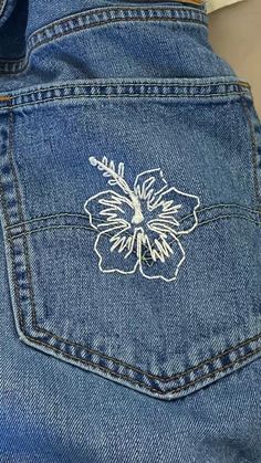 the back pocket of a pair of jeans with embroidered flowers on each side and white stitching