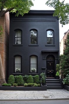 a black house with many windows and bushes on the sidewalk in front of it's entrance