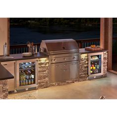 an outdoor kitchen with stainless steel appliances and stone counter tops, overlooking the water at night