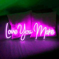 two pillows with the words love you more lit up in purple light on a couch