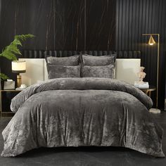 a bed with grey comforter and pillows in a black walled room next to a plant