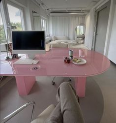 a pink desk with a computer monitor and keyboard on it in front of a large window