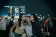 three girls are posing for the camera in front of a cityscape at night