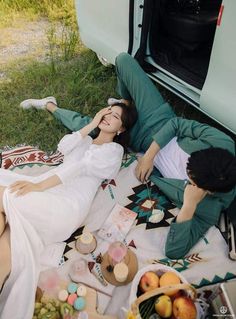 two people laying on the ground next to a van with food and drinks in it