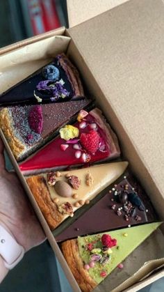 a person holding an open box filled with different types of desserts on top of each other