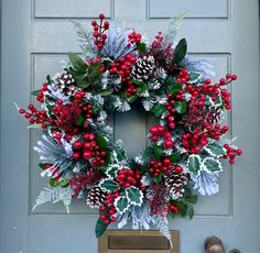 a christmas wreath with holly, berries and pine cones is hung on the front door