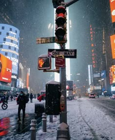 a street sign on a pole in the middle of a snow covered city at night