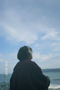 a man sitting on top of a bench next to the ocean under a cloudy blue sky