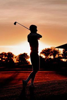 a person swinging a golf club at sunset