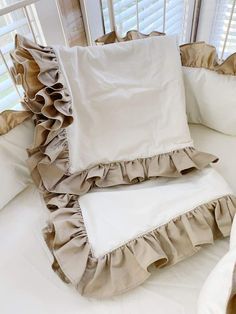 two pillows with ruffled edges sit on a white couch in front of blinds and windows