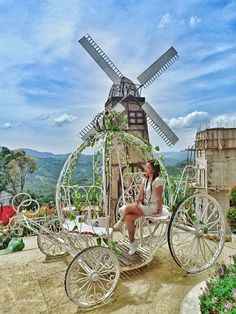 a woman is sitting in a carriage with a windmill behind her on top of a hill