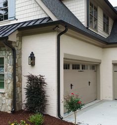 a white brick house with two garages and flowers in the front yard, on a cloudy day