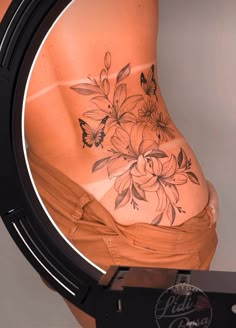 a woman's stomach with flowers and butterflies painted on the side of her body